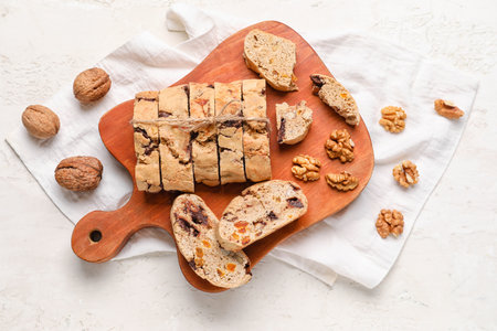 Wooden board with tasty biscotti cookies and walnuts on light backgroundの写真素材