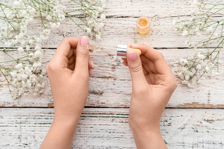 Female hands with cuticle oil and gypsophila flowers on light wooden background, closeupの写真素材