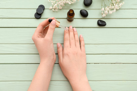 Female hands with bottle of cuticle oil, spa stones and gypsophila flowers on color wooden backgroundの写真素材