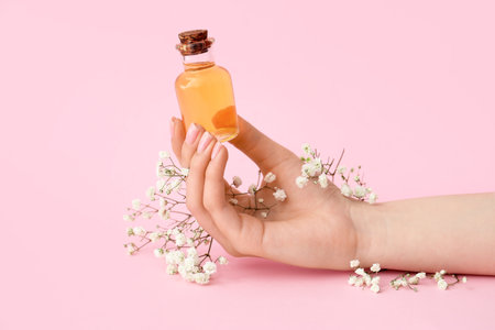 Female hand with bottle of cuticle oil and gypsophila flowers on color backgroundの写真素材