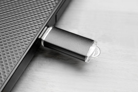 Modern laptop with black USB flash drive on white wooden background
