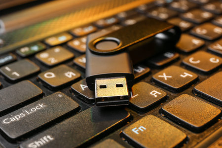 Black USB flash drive on modern laptop, closeup