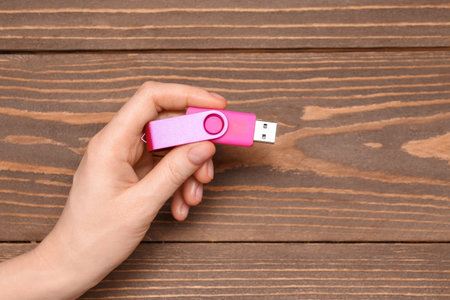 Woman holding pink USB flash drive on wooden background