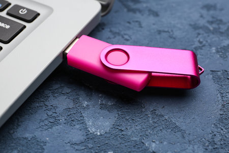 Modern laptop with pink USB flash drive on blue grunge backgroundの写真素材