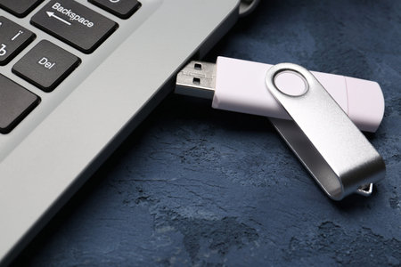 Modern laptop with white USB flash drive on blue grunge background