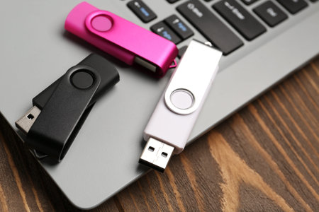 USB flash drives and laptop on wooden background, closeup
