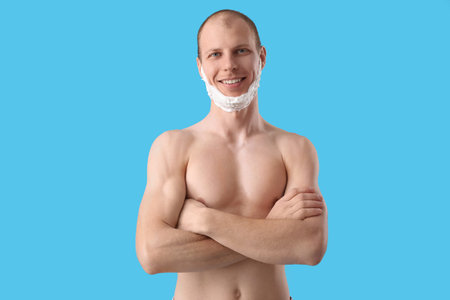 Young man with shaving foam on face against light blue backgroundの写真素材