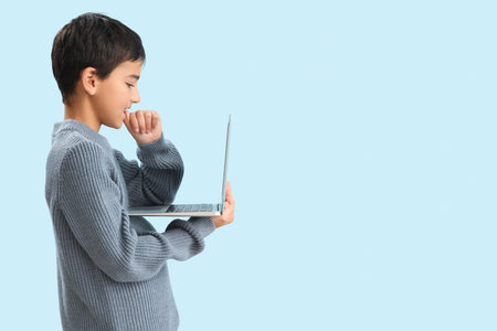 Little boy with laptop biting nails on blue backgroundの写真素材