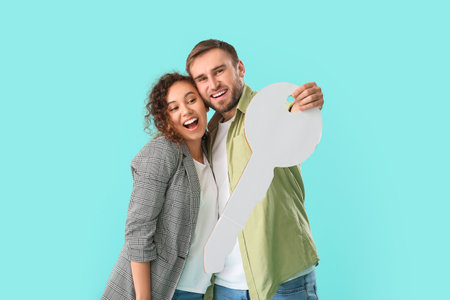 Happy young couple with big paper key on color backgroundの写真素材