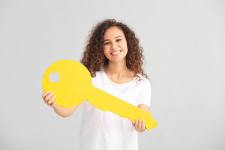 Young woman with big paper key on gray backgroundの写真素材