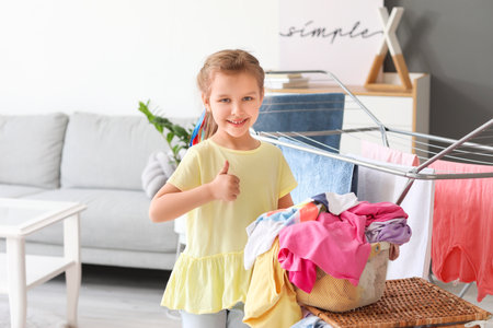 Little girl with dirty laundry showing thumb-up at homeの写真素材