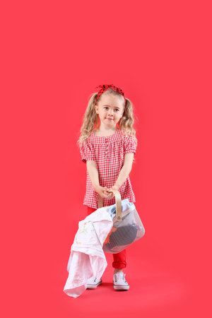 Cute little girl with dirty laundry on color backgroundの写真素材