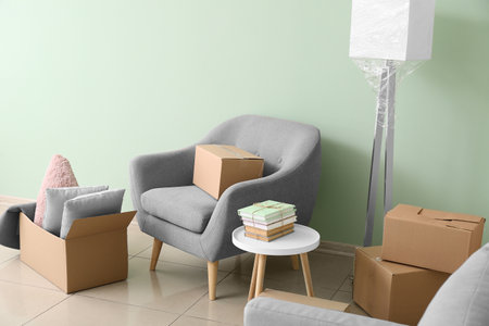 Cardboard boxes with accessories and armchair in new flat on moving dayの写真素材