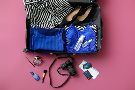 Open packed suitcase and accessories on color background
