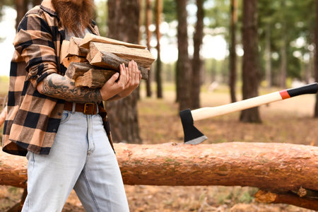 Handsome lumberjack with tree logs in forestの写真素材