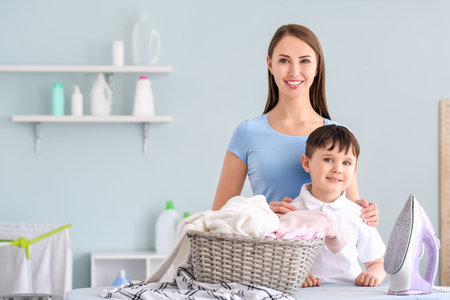 Young woman with her little son ironing laundry at homeの写真素材