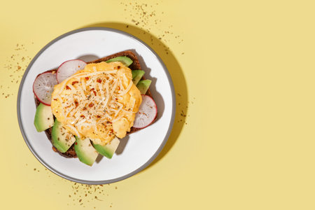 Plate with tasty scrambled eggs sandwich and vegetables on yellow backgroundの写真素材