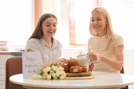 Mature woman with her daughter drinking tea in the kitchen. mother's day celebrationの写真素材