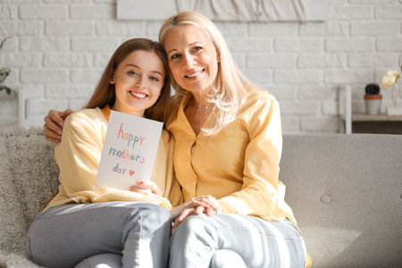 Young woman greeting her mother with card at homeの写真素材