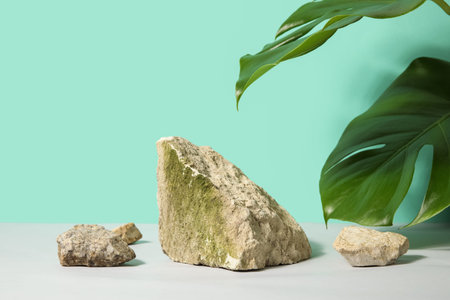 Stones and monstera leaves on white table against turquoise background