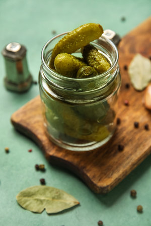 Jar with tasty fermented cucumbers and wooden board on green backgroundの写真素材