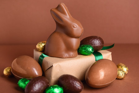 Chocolate Easter eggs, bunny and gift box on brown background