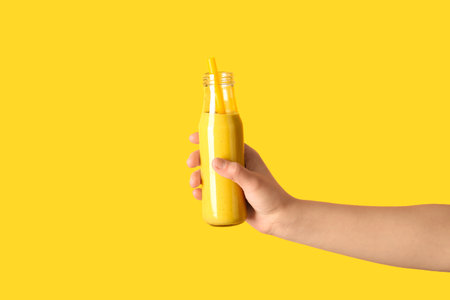 Female hand with glass bottle of yellow smoothie on color backgroundの写真素材