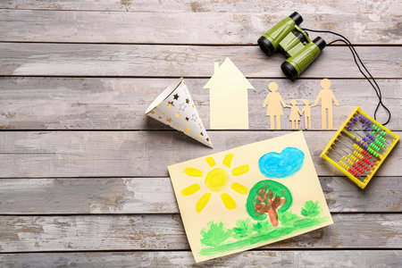 Family figure with paper house, drawing, toys and party hat on wooden background. Children's Day celebrationの写真素材