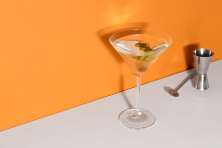 Glass of martini with olives, bar spoon and jigger on color backgroundの写真素材