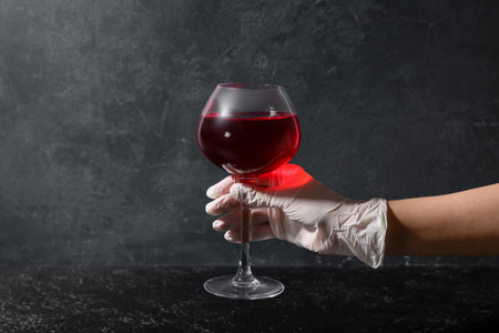 Woman in rubber glove with glass of red wine on dark backgroundの写真素材