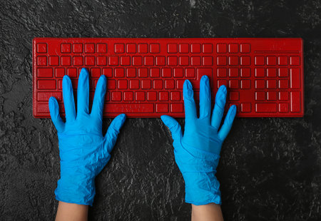 Woman in rubber gloves with computer keyboard on dark backgroundの写真素材