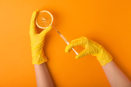 Woman in rubber gloves with syringe and orange slice on color backgroundの写真素材