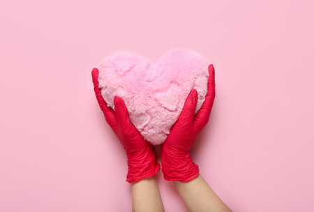 Woman in rubber gloves with heart pillow on pink backgroundの写真素材