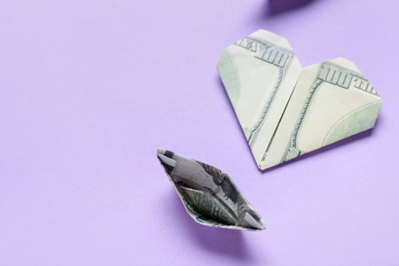 Origami boat and heart made of dollar banknotes on lilac backgroundの写真素材
