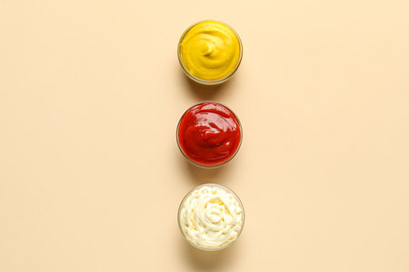 Bowls of ketchup, mayonnaise and mustard on beige backgroundの写真素材