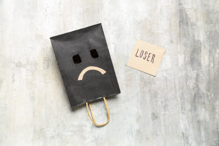 Paper bag with sad smile and word LOSER on grunge background