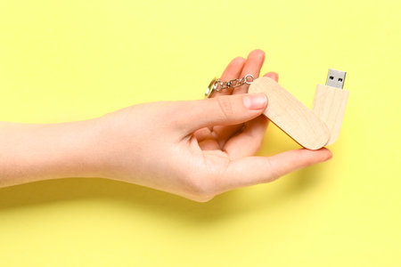 Woman holding wooden USB flash drive on yellow backgroundの写真素材