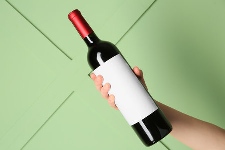 Female hand holding bottle of red wine on green backgroundの写真素材