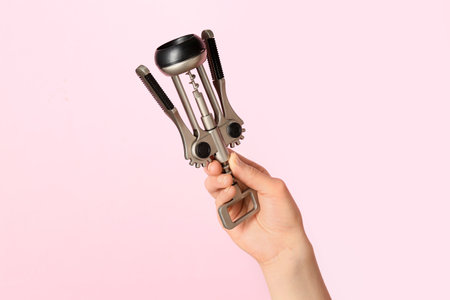 Female hand holding wine opener on pink backgroundの写真素材