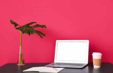 Workplace with laptop, notebook, cup of coffee and palm leaf near red wallの写真素材