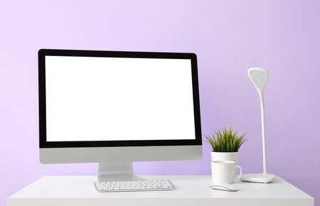 Workplace with computer, cup and lamp near lilac wall