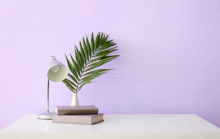Workplace with lamp, books and palm leaf near lilac wallの写真素材