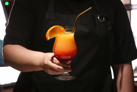 Female bartender holding glass of tasty Tequila Sunrise in barの写真素材