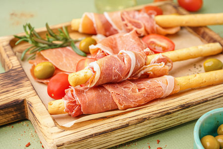 Wooden board of tasty Italian Grissini with jamon on green background, closeupの写真素材