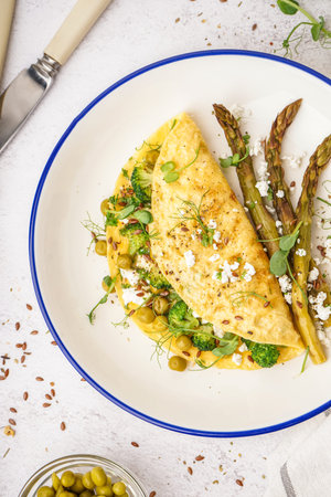 Tasty omelet with broccoli, asparagus and pea on light table