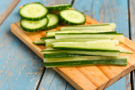 Board with fresh cut cucumber on blue wooden background, closeupの写真素材