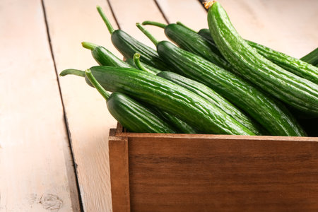 Box with fresh cucumbers on light wooden background, closeupの写真素材