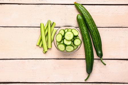 Bowl with cut and whole cucumbers on light wooden backgroundの写真素材