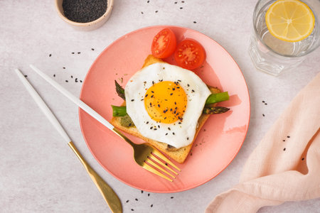 Delicious sandwich with fried egg, asparagus and tomatoes on gray background