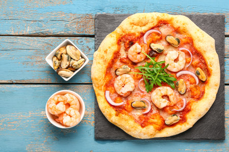 Slate board with tasty seafood pizza and ingredients on blue wooden backgroundの写真素材